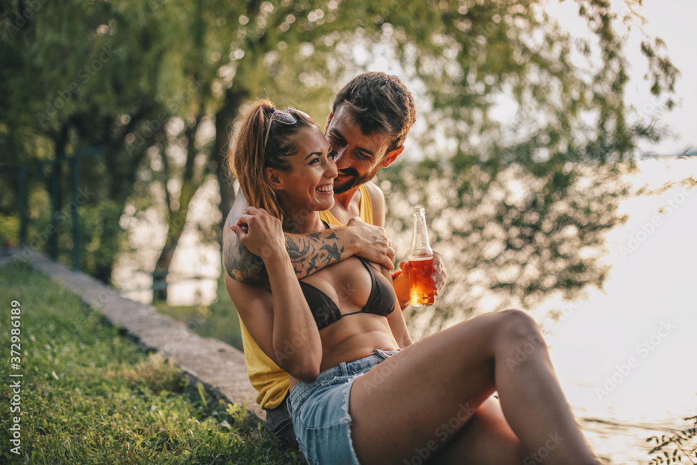 Fototapeta premium A beautiful handsome couple during the day has love moments by the river, man has a bottle in his left hand