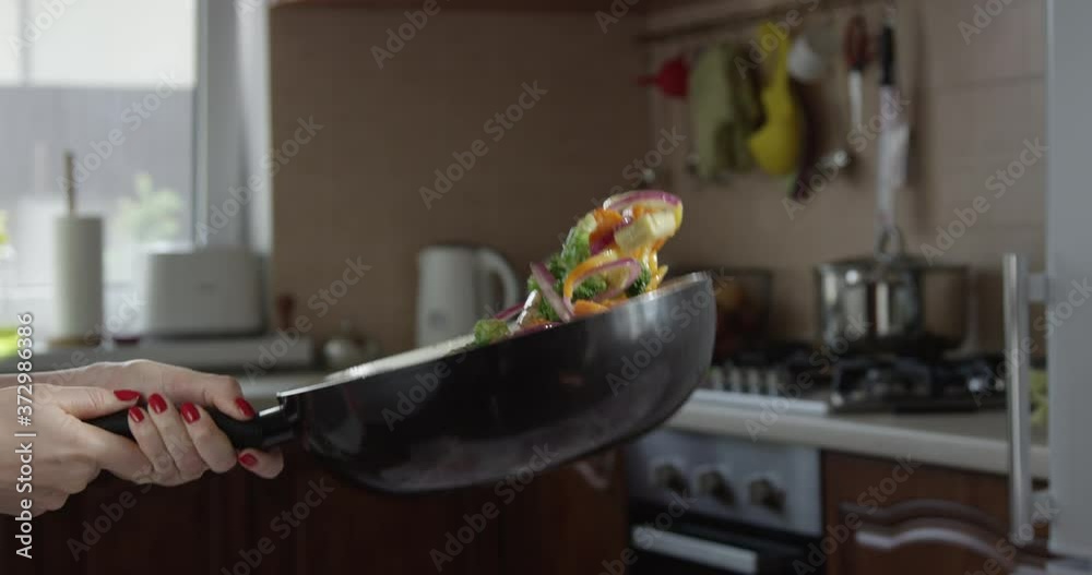 Woman Tossing Vegetables on a Frying Pan in the Kitchen in Slow Motion Shot on Red Camera Woman Tossing Vegetables on a Frying Pan in the Kitchen in Slow Motion Shot on Red Camera