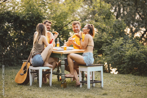Two couples sit outside in nature, enjoying themselves, eating pizza and drinking beer photo