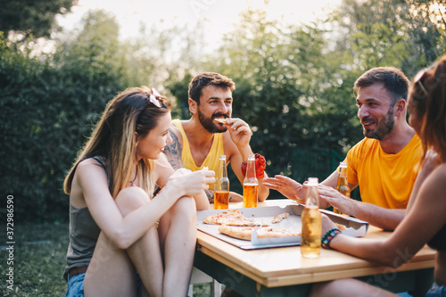 Two couples sit outside in nature, enjoying themselves, eating pizza and drinking beer