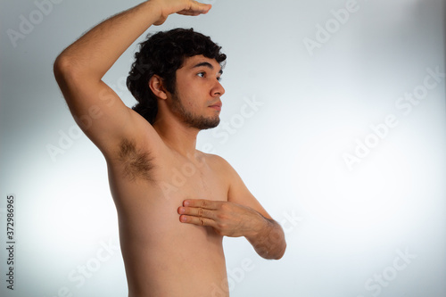 Young naked hispanic man with wavy hair and shaved beard, doing a checkup on his chest for signs of breast cancer