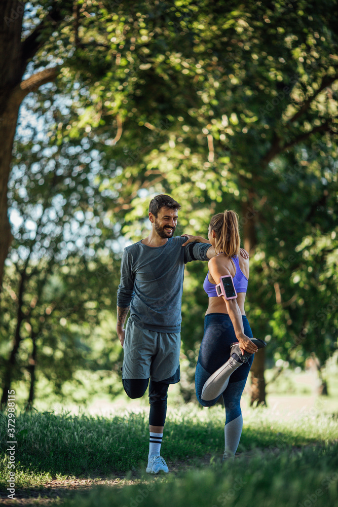 Side image of a young couple doing warming exercise in nature, they smiling and stick each other to maintain balance