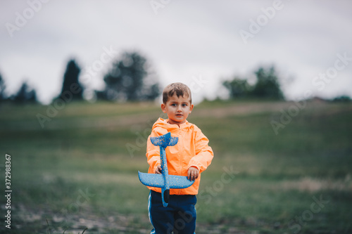 Boy stands on a meadow and holds a toy airplane in his hands