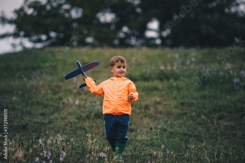 The boy stands alone in the meadow, smiling and holding a toy airplane in his hand