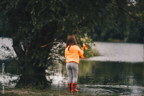 Fototapeta Naklejka Na Ścianę i Meble -  A picture from behind of a girl standing in a river holding her toy in her hand