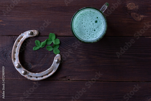 Green Shamrocks clovers on wooden table with a large mug of beer and a gold horseshoe.