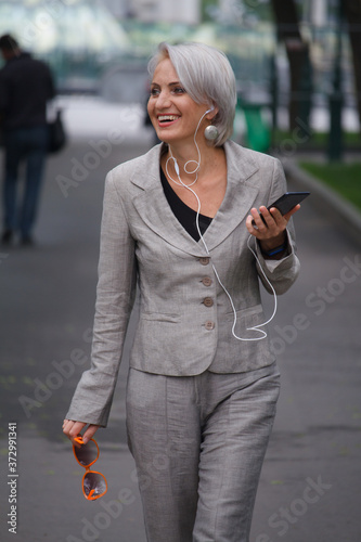 Photography Mature blonde woman walks in public park, listens to music with headphones and s