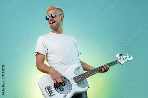 Cheerful hipster man play white bass guitar in neon lights. Rock music concept. Rock star.