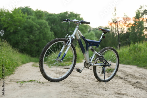 beautiful mountain bicycle is on sand road on green nature background at sunset