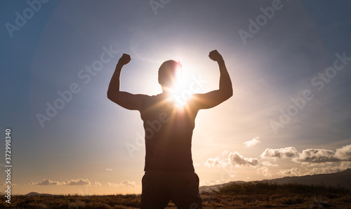 Strong confident man flexing facing the sunrise on a mountain. People power and motivation concept.  photo