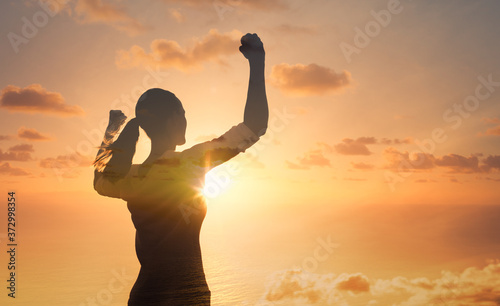 Young female against sunrise with fist in the air feeling strong and confident. Victory and success concept.	