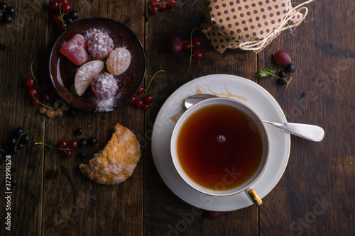 Summer breakfast. Vintage cup of tea with gold decoration and figured marmalade on the old wooden table on which berries lie