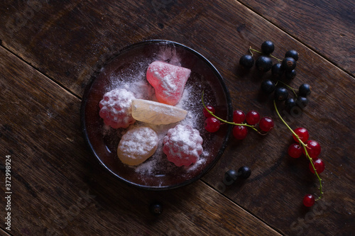 Black plate with figured colorful marmalade and currant on the old wooden table