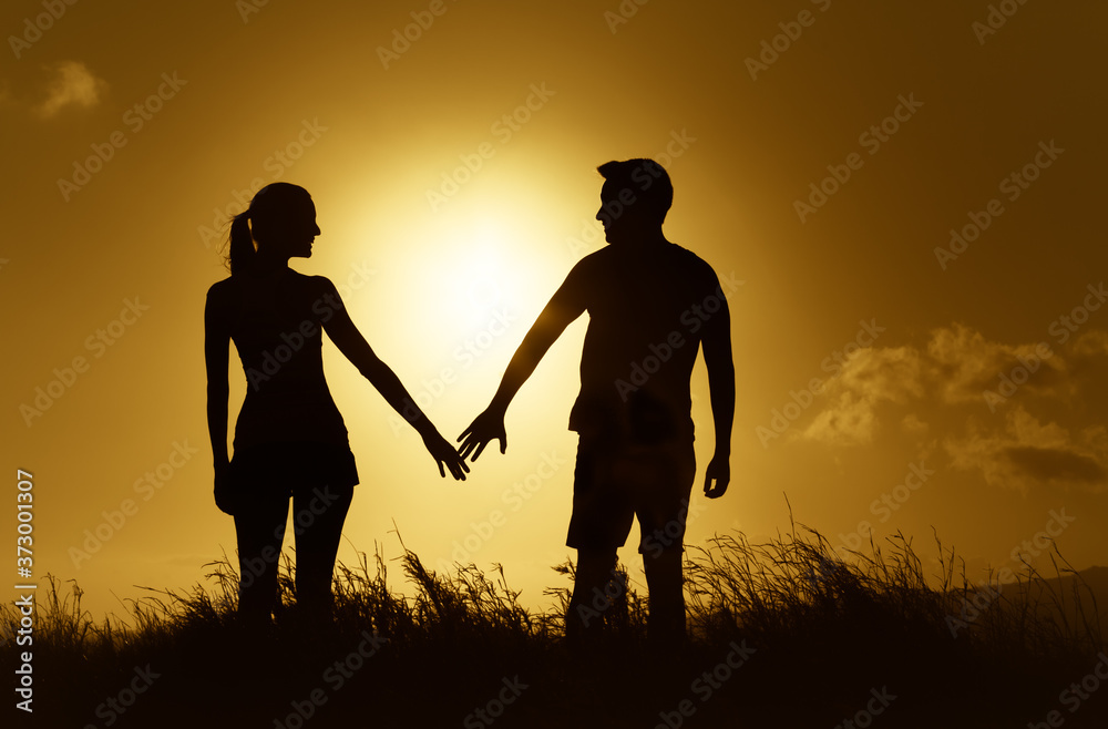 Man and woman joining hands standing together in a meadow at sunset. 