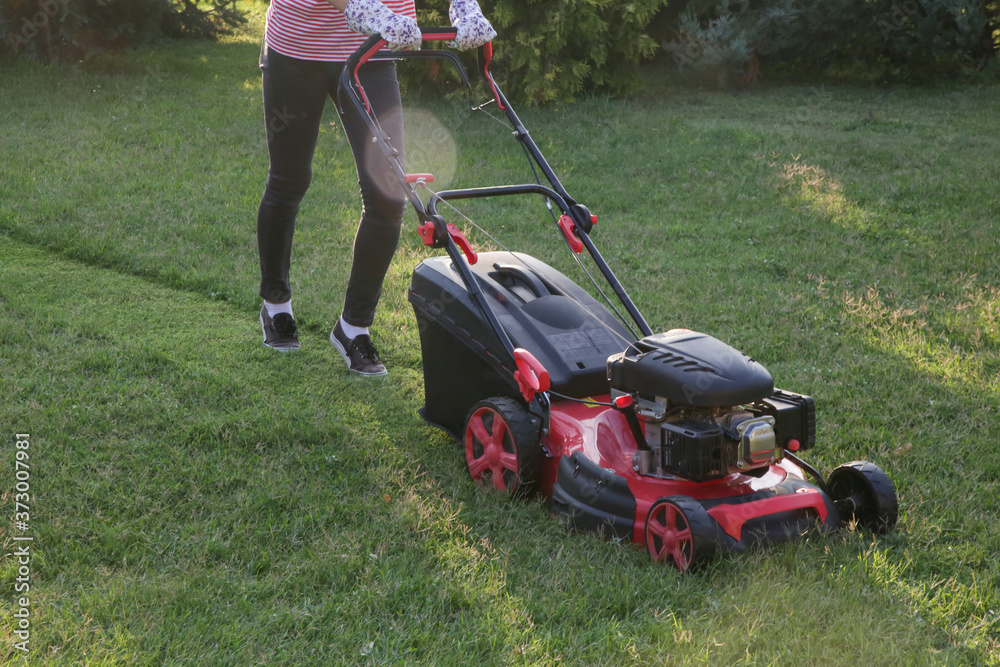 Young woman cutting grass with a lawn mower. Outdoor household chores concept. Young woman cutting grass with a lawn mower. Outdoor household chores concept.