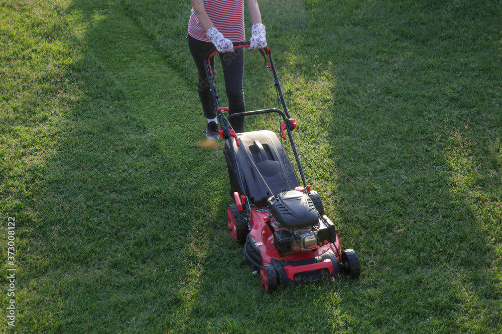 Young woman cutting grass with a lawn mower. Outdoor household chores concept. Young woman cutting grass with a lawn mower. Outdoor household chores concept.
