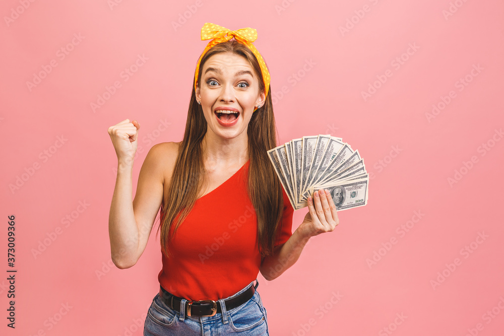 Portrait of a cheerful young woman holding money banknotes and celebrating isolated over pink background. Portrait of a cheerful young woman holding money banknotes and celebrating isolated over pink background.