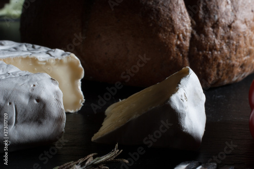 Close up of Fresh French Brie cheese and a one slice on a black stone plate with bread © Mitya Pylaev