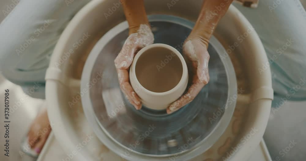 Woman makes clay bowl in studio on pottery wheel, up-close hands and clay, top view, handmade