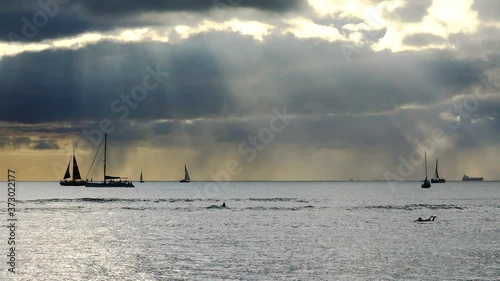 Sailboats and surfers at sunset from Waikiki Beach, Oahu, Hawaii.