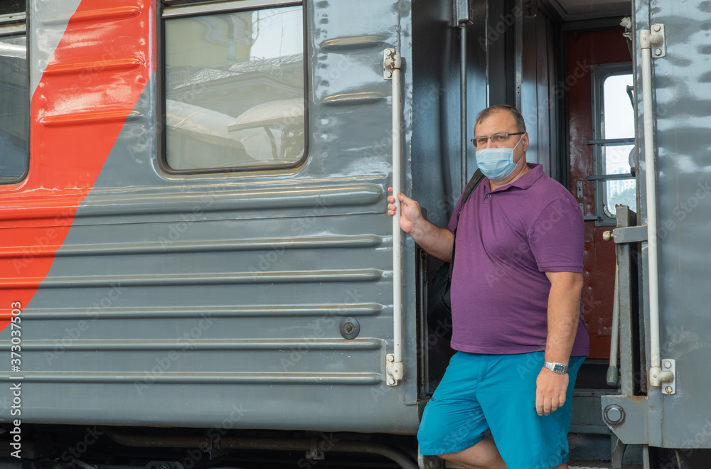 man in a medical mask near the train car. concept of travel during the pandemic. mode of permanent wearing of a protective medical mask. man in a medical mask near the train car. concept of travel during the pandemic. mode of permanent wearing of a protective medical mask.