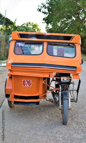 An empty orange tricycle is parked at the side of a concrete road in Coron, Palawan