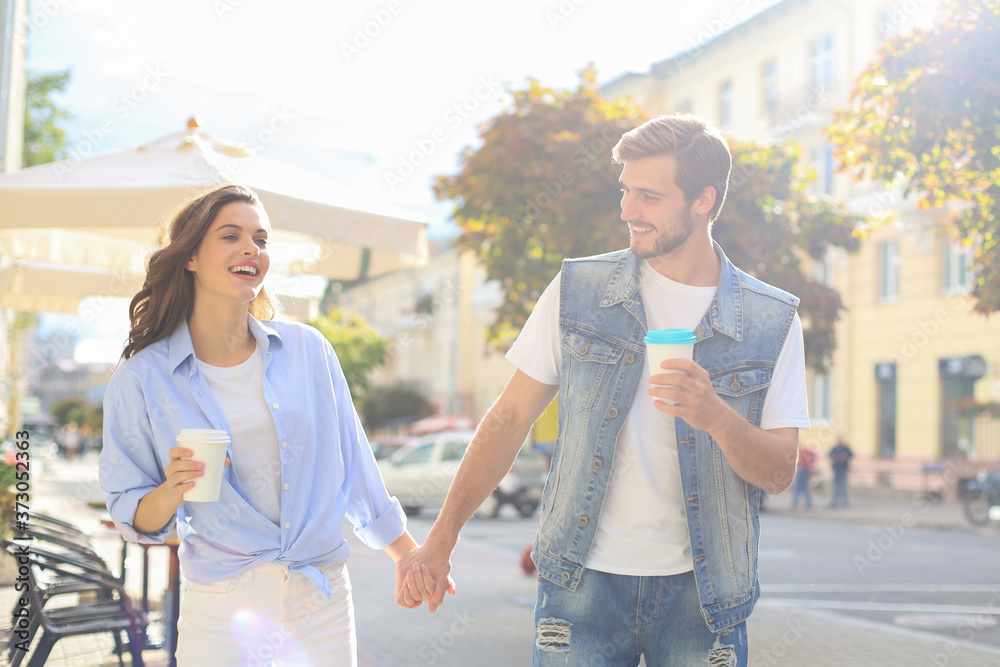 Image of lovely happy couple in summer clothes smiling and holding hands together while walking through city street.