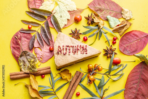 Piece of tasty mousse cake with the word Autumn, laid from dried berries. Yellow leaves and berries lie nearby. Concept of time of year