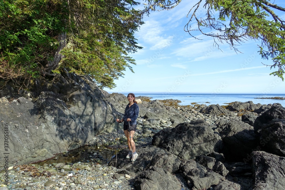 A female hiker exploring the sandy beaches of nels bight and experimental bight, surrounded by forest and the pacific ocean, along the beautiful cape scott trail on Northern Vancouver island