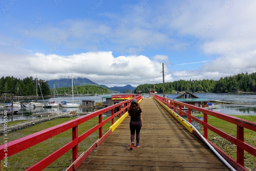 A woman walking along a dock at the harbour in Tofino, overlooking the beautiful ocean and islands in the background, in Tofino, Canada. A woman walking along a dock at the harbour in Tofino, overlooking the beautiful ocean and islands in the background, in Tofino, Canada.