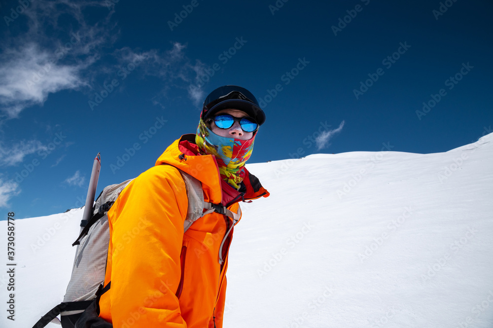 Portrait of a stern climber skier in sunglasses and a cap with a ski mask on his face. against the backdrop of Mount Elbrus Portrait of a stern climber skier in sunglasses and a cap with a ski mask on his face. against the backdrop of Mount Elbrus
