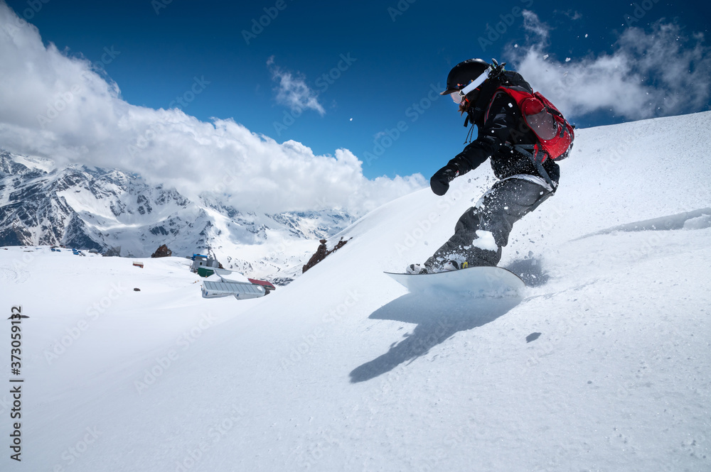 Girl snowboarder with a backpack on a snowy fresh slope against the backdrop of high mountains and blue sky. Winter kinds of extreme sports. Snowboard