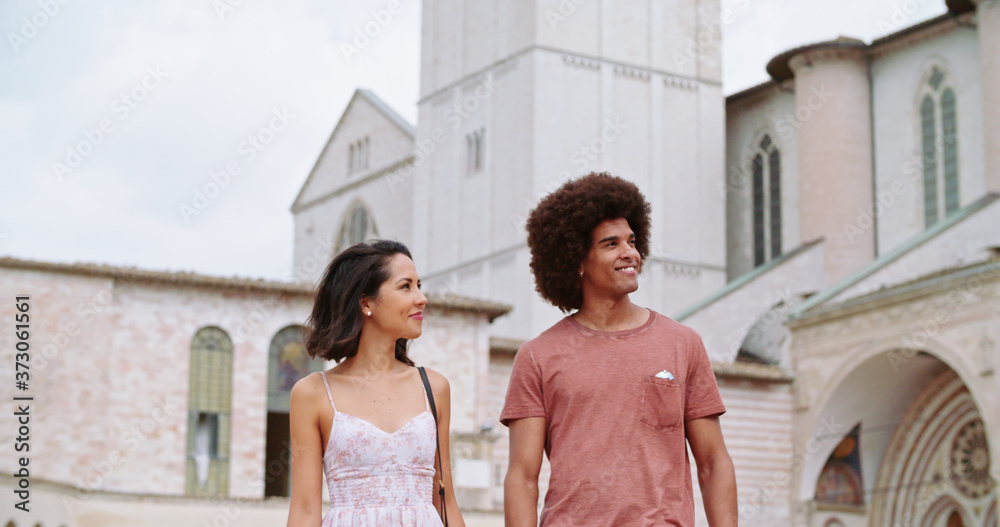 Two people walking together smiling in sunny day. Man and woman walking and smiling.Romantic couple walking with bell tower in background. Handheld Slow motion close shot.Friends trip in Italy.