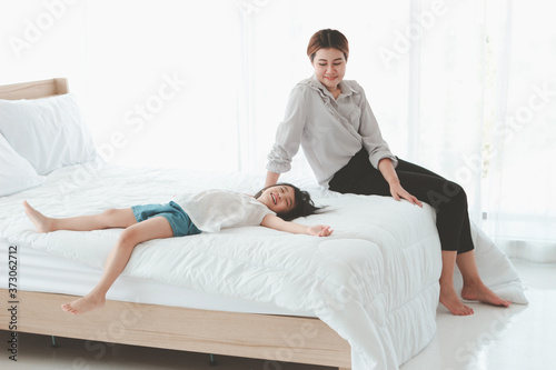 Happy family having fun at house. Mother and daughter spending time together, little girl lying down in bed, your mother sits next to her, parent and kid having good memory together at home