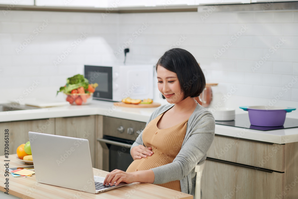 Profile side view attractive and progressive young mama sitting in chair behind table inside bright flat and using pc laptop