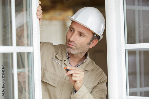 male glazier holding screwdriver by open pvc window