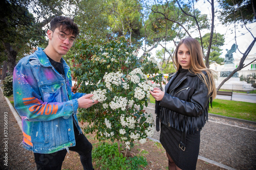 Outdoor, a young italian man and woman are couple in spring day in the park look over the hedge at the park flowers whit three and green whit flower photo