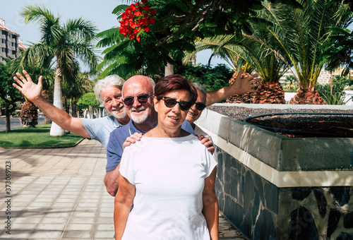 Group of four smiling senior and mature people enjoying the sunny day in public park with palm trees - concept of active elderly during vacations