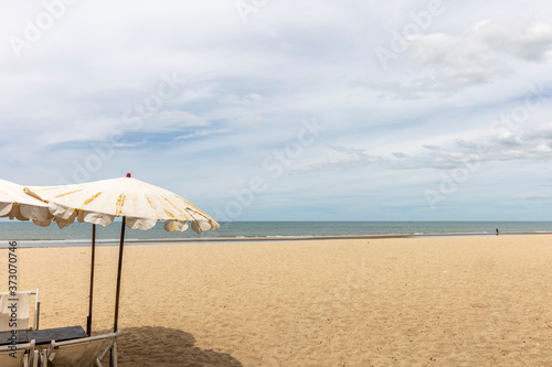 Beach umbrella at foreground. Scenic view of empty tropical sandy and peaceful beach under cloudy blue sky with light turquoise waves.