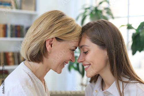 Cheerful young woman is embracing her middle aged mother in living room.
