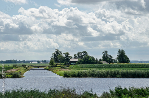 Kampen, The Netherlands, July 26, 2020: landscape with a small lake lined with reeds, trees, farms and meadows under a dramatic sky