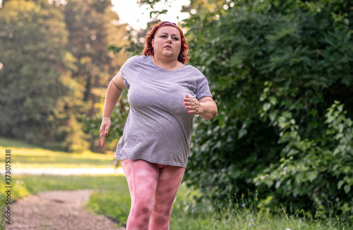 An obese woman jogging in nature on a sunny day, doing weight loss training