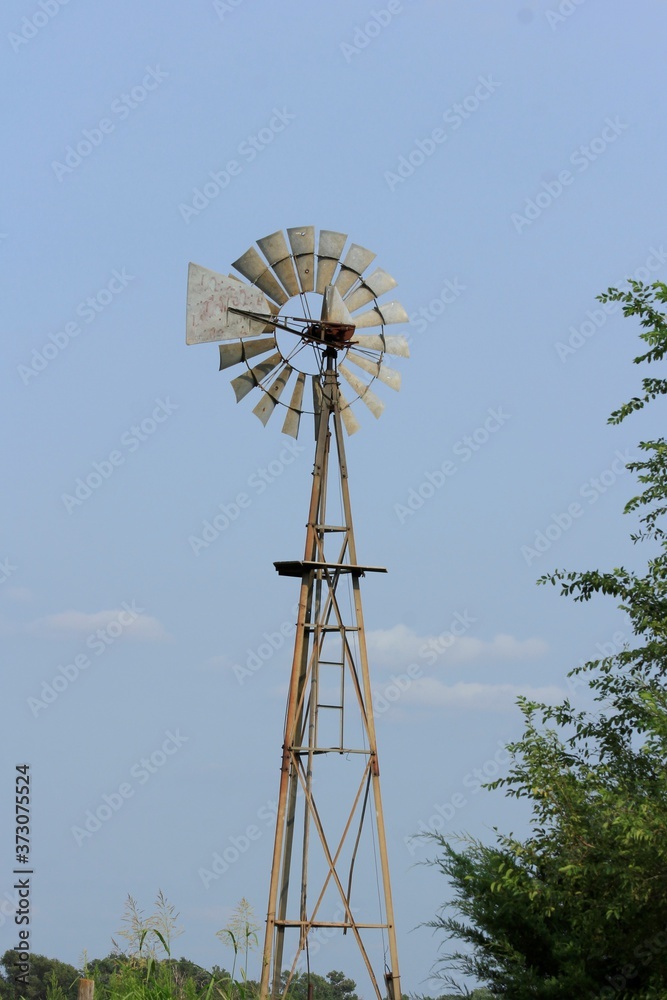 old windmill in the field with tree's and blue sky with tree's in Kansas. old windmill in the field with tree's and blue sky with tree's in Kansas.