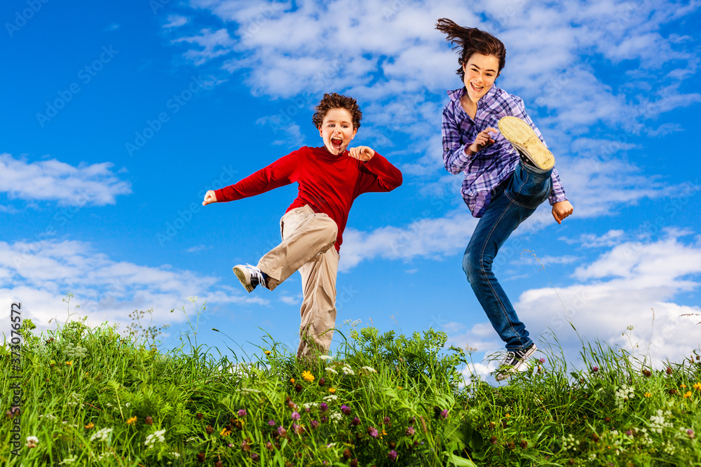 Girl and boy running, jumping against blue sky
Girl and boy running, jumping against blue sky