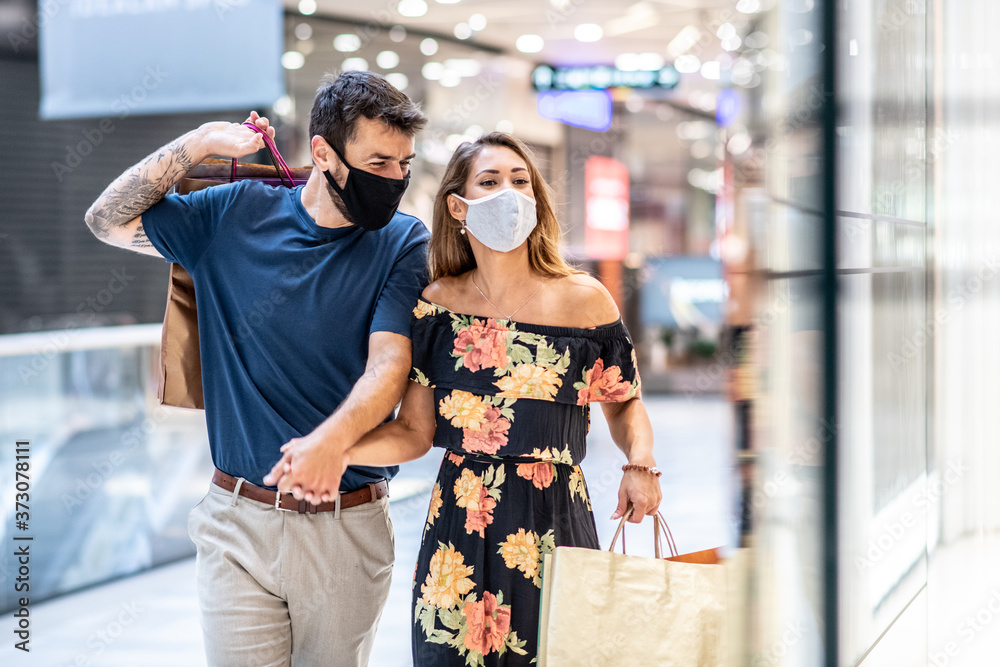 A young couple is carrying shopping bags with masks on their faces and walks, shopping during a pandemic A young couple is carrying shopping bags with masks on their faces and walks, shopping during a pandemic