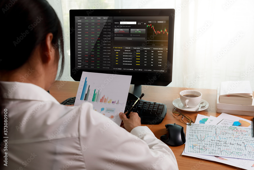 Rear view of businesswoman working in office with computer holding chart report paper and looking. businesswoman analysis project statistics data on PC screen and paper. Business and finance concept. Rear view of businesswoman working in office with computer holding chart report paper and looking. businesswoman analysis project statistics data on PC screen and paper. Business and finance concept.