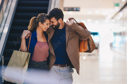 A man with bags in his hand in an embrace with his wife walk contentedly through a shopping mall