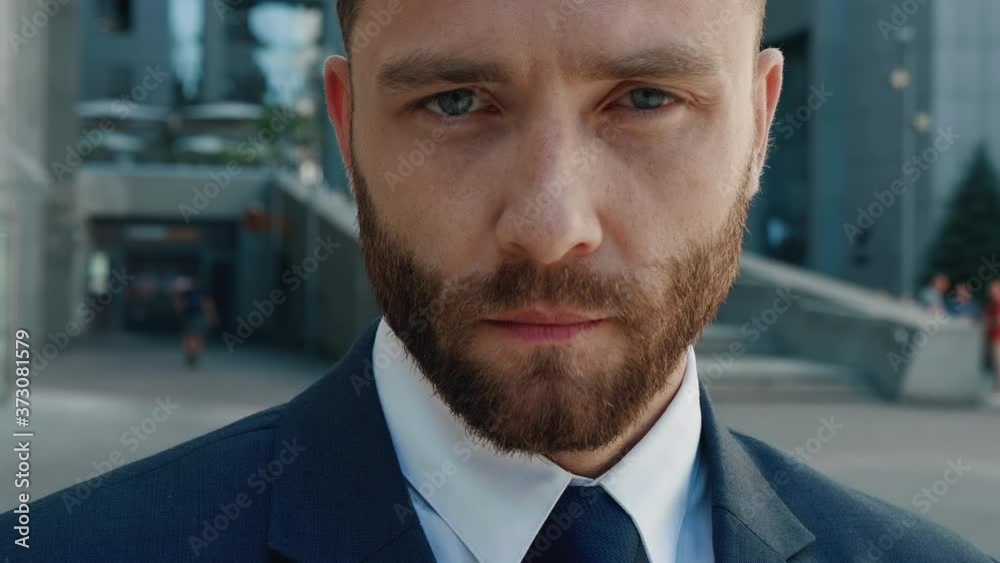 Close-up Portrait of Attractive Bearded Business Man Entrepreneur looking Serious at Camera Ambitious Male Leadership. Confident Boss Businessman on the Background of the Business District. Steadicam. Close-up Portrait of Attractive Bearded Business Man Entrepreneur looking Serious at Camera Ambitious Male Leadership. Confident Boss Businessman on the Background of the Business District. Steadicam.