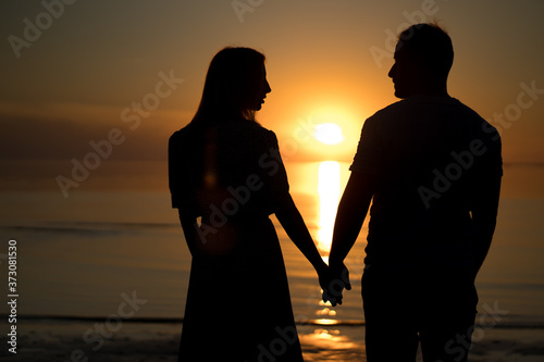 silhouette of couple on the beach. Beautiful sunset of bright red orange color. Background for the travel website screensaver.