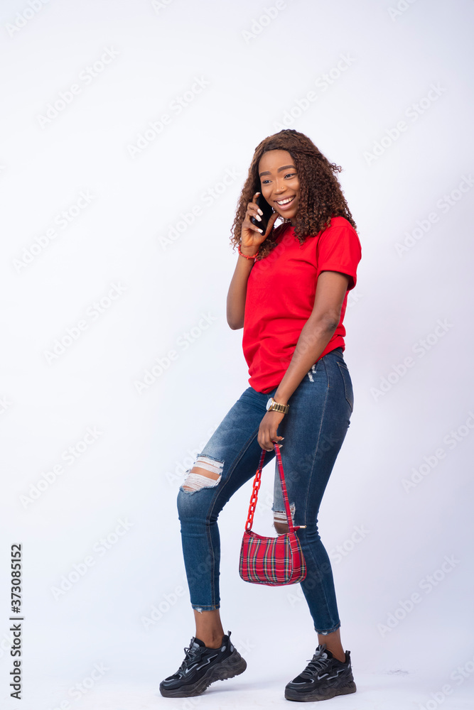 pretty young african woman wearing red top and blue jeans, carrying a handbag making a phone call pretty young african woman wearing red top and blue jeans, carrying a handbag making a phone call